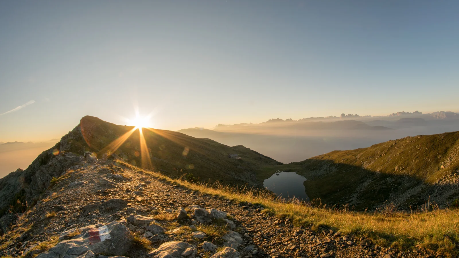 A stony mountain trail at sunrise, the sun breaking low over the ridge ahead